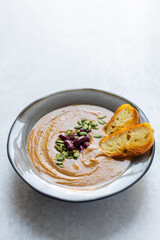 Healthy vegan pumpkin soup with red beans, pumpkin seeds, coconut cream and slices of fried bread