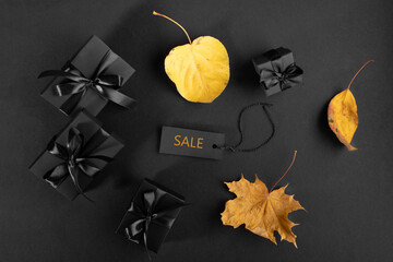 Flat lay arrangement of black wrapped gift boxes with yellow fall leaves and sale tag on black.