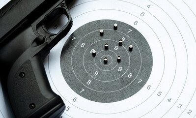 Black air gun pellet gun laying on a paper shooting target next to a bunch of steel metal pellets...