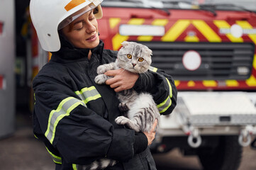 Conception of savior. Holding cat in hands. Woman firefighter in uniform is at work in department