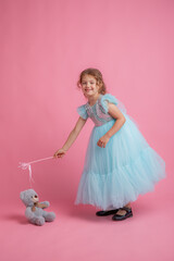 cute little girl in a beautiful dress holding a fairy magic wand on a pink background