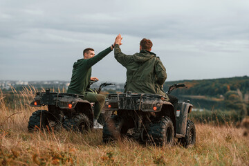 Obraz premium Beautiful landscape, giving high five. Two men are on the quad bikes outdoors on the field