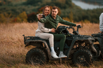 Fototapeta premium Making a selfie. Lovely young couple is with quad bike outdoors on the field