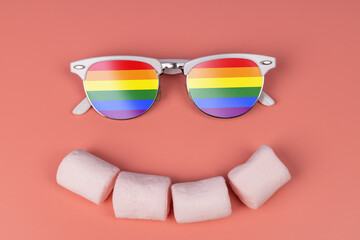 Emoticon on a pink background. Marshmallow smile and glasses on the eyes. Wearing LGBT rainbow glasses. LGBT concept