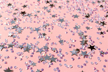 Glowing silver stars and crystals confetti on a pink background. Selective focus.