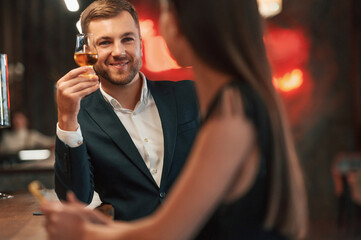 Smiling, talking with each other. Man and woman are sitting at the bar with drink