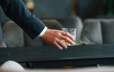 Close up view of man's hand that taking glass of alcohol drink from the table - obrazy, fototapety, plakaty