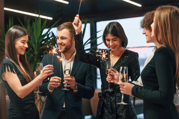 With new year sparklers. Group of people in beautiful elegant clothes are indoors together