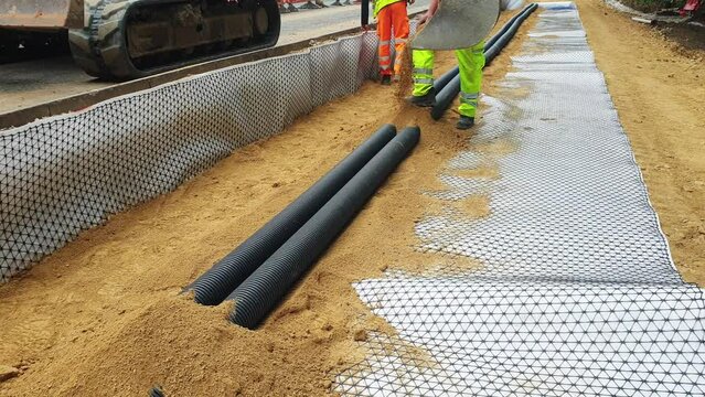 Groundworkers installing new electric ducts during roadworks on construction site	