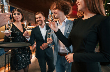 Taking glasses with champagne. Group of people in beautiful elegant clothes are celebrating New Year indoors together