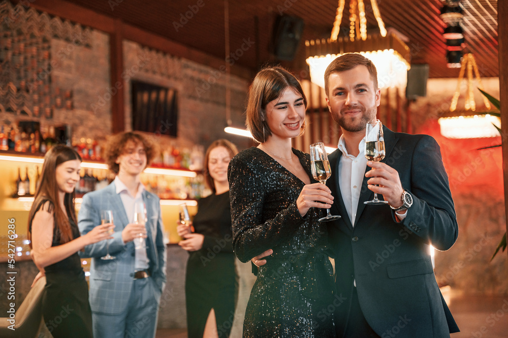 Wall mural Man with woman is posing. Group of people in beautiful elegant clothes are celebrating New Year indoors together