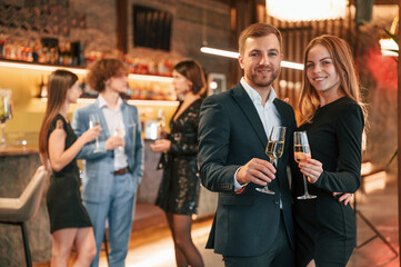 Man with his woman is standing and smiling. Group of people in beautiful elegant clothes are celebrating New Year indoors together