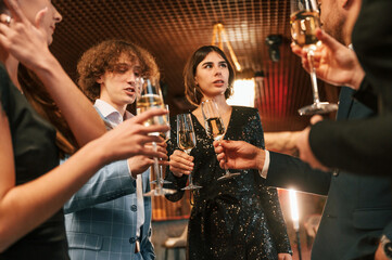 Holding glasses with champagne. Group of people in beautiful elegant clothes are celebrating New Year indoors together
