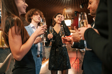 Holding glasses with champagne. Group of people in beautiful elegant clothes are celebrating New Year indoors together