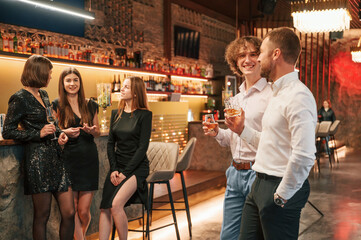 Two men are standing at the party together with alcohol drinks in hands
