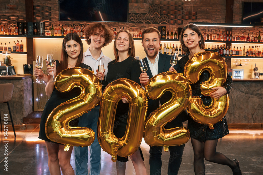 Wall mural with 2023 numbers balloons. group of people in beautiful elegant clothes are celebrating new year in