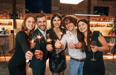 Champagne and sparklers. Group of people in beautiful elegant clothes are celebrating New Year...