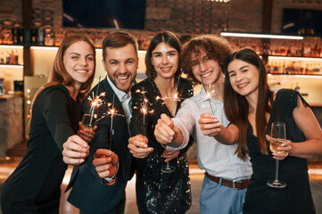 Champagne and sparklers. Group of people in beautiful elegant clothes are celebrating New Year indoors together