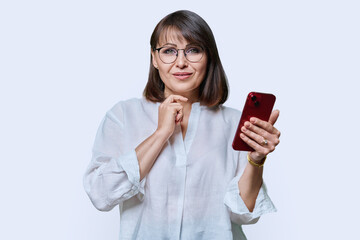 Portrait of middle aged woman with phone looking at camera on white background