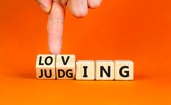 Loving or judging symbol. Concept words Loving or Judging on wooden cubes. Businessman hand. Beautiful orange table orange background. Business loving or judging concept. Copy space.