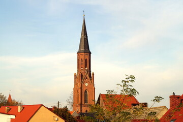 In the photo, among the roofs of houses, the spire of the church tower with a cross, against the background of a blue sky. horizontal photo taken in the city of Lubniewice in Poland