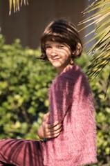 portrait of a female child short brown hair, kiss,  pink sweater, tree leaves background