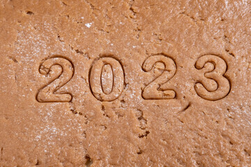 Fototapeta na wymiar The figures of the year 2023 are cut out of gingerbread dough for Christmas cookies. Cooking homemade gingerbread. Cut out the New Year's date from the rolled dough