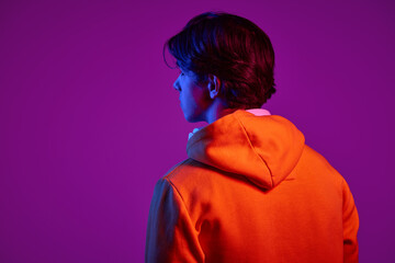 Portrait of young man in casual hoodie posing isolated over purple background in neon light. Back view