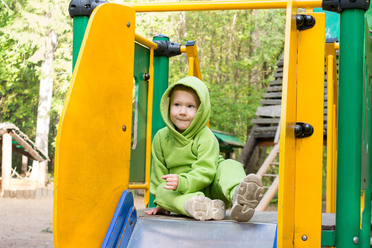 A child, a little girl dressed in a green hoodie, plays in the playground on a summer day.