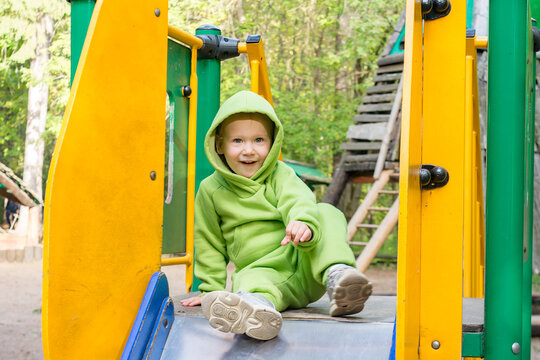 A child, a little girl dressed in a green hoodie, plays in the playground on a summer day.