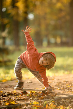 A Little Boy Rides A Skateboard In The Park In The Fall