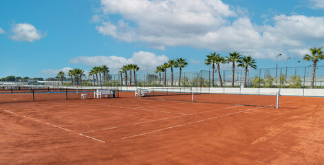 Baseline and net of an empty clay tennis court on a sunny day