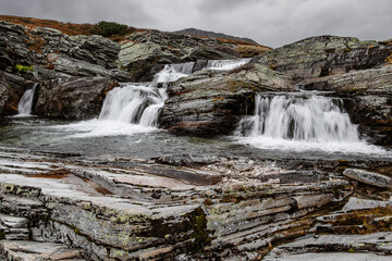autumn mountain landscape of Rondane National Park in Norway, waterfall on small river