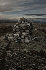 dark moody landscape cairn stack of stones on top of a mountain at dusk