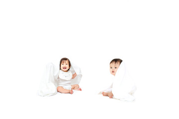 白背景の前に座りバスタオルを被り遊ぶ2人の女の子の赤ちゃん