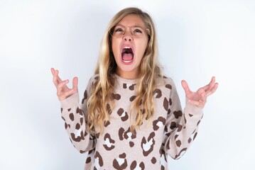 beautiful caucasian teen girl wearing animal print sweater over white wall crying and screaming....