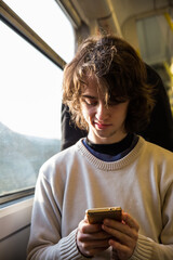 Young little teenager boy using cellphone while sitting in a train .