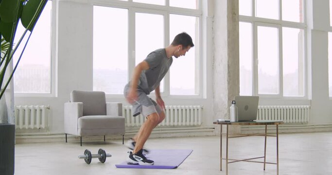 Athletic fitness coach in sportswear showing how to train at home while providing online lesson via laptop