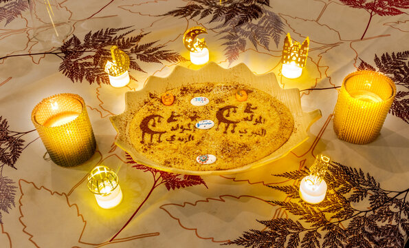 A homemade tamina plate decorated with crescent moons, candles and arab inscriptions saying el mawlid el nabawi el charif happy prophete's birthday of 2022. Directly above view.