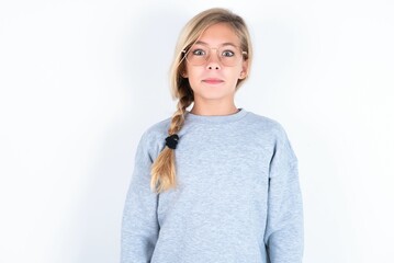 Stunned beautiful caucasian teen girl wearing gray sweater over white wall stares reacts on...