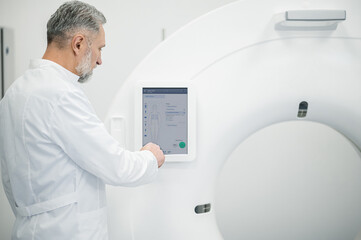Mature radiologist standing near medical equipment and looking busy