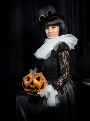A beautiful brunette in a vintage black dress, a white frill and a vintage hat holds a scary...