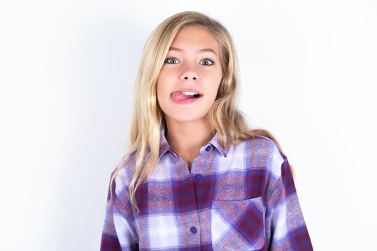 Beautiful Caucasian Teen Girl Wearing Plaid Purple Shirt Over White Wall Showing Grimace Face Crossing Eyes And Showing Tongue. Being Funny And Crazy