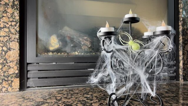 Artificial candles on candlesticks glow against the background of a fireplace all in a web a spider sits on them trick or treat halloween decoration The wind blows the web develops scary and creepy