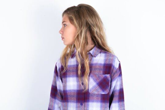 Close up side profile photo beautiful caucasian teen girl wearing plaid purple shirt over white wall not smiling attentive listen concentrated