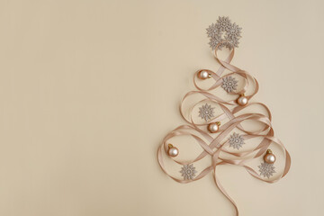 Top view of baubles balls, stars and ribbons arranged in Christmas tree with toys on pastel beige...
