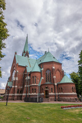 Fototapeta na wymiar Finland, Kotka - July 18, 2022: Kotka-Kymin Parish Church or Seurakuntayhtymä. NW corner view on red brick walls, clock tower and green roofs. Lawn with red flowers