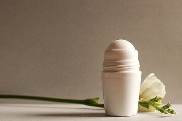 White roll-on antiperspirant deodorant bottle on a gray background with freesia branch. Skin care concept. Copy space.