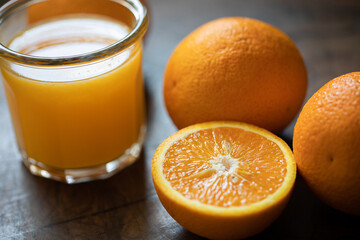 Glass of orange juice and oranges on a wooden table. Backlight. Close up