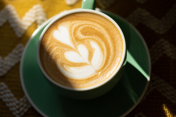 Cappuccino with latte art in a green cup in hard light. Close up.